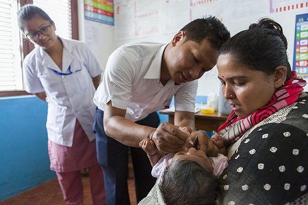 Nanu Sharma receives one of several vaccines at the Tathali health post, as mother Anju looks on. Bhaktapur District, Nepal. August 2019